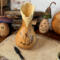 This shows a gourd with a butterfly wood burned onto the front. The top is carved into a wavy rim. Mushroom gourds sit in the background. 